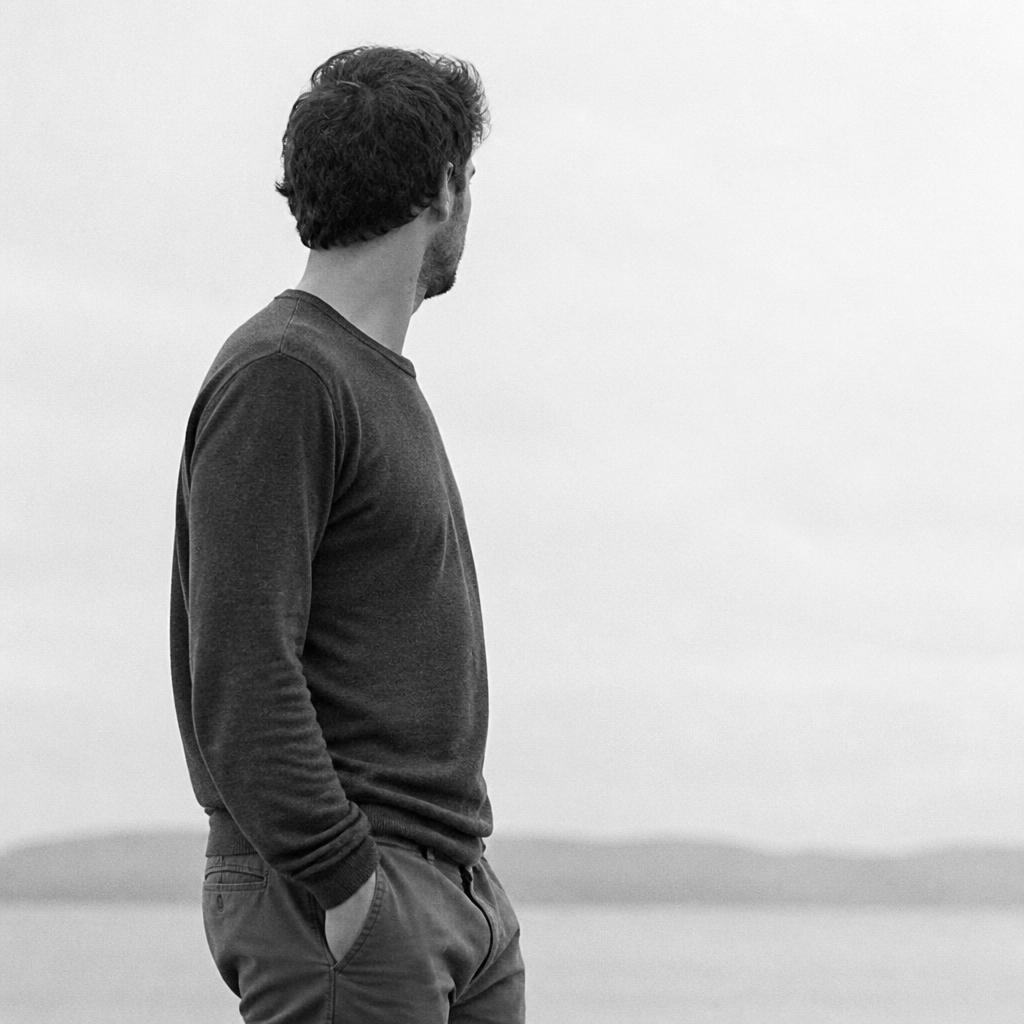 A man standing outdoors with his back half turned, looking away